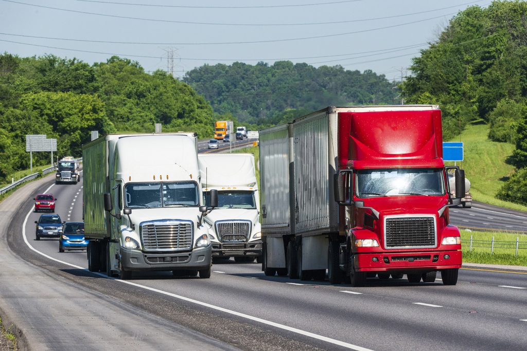 Three large semi-trucks crowd an Interstate Highway